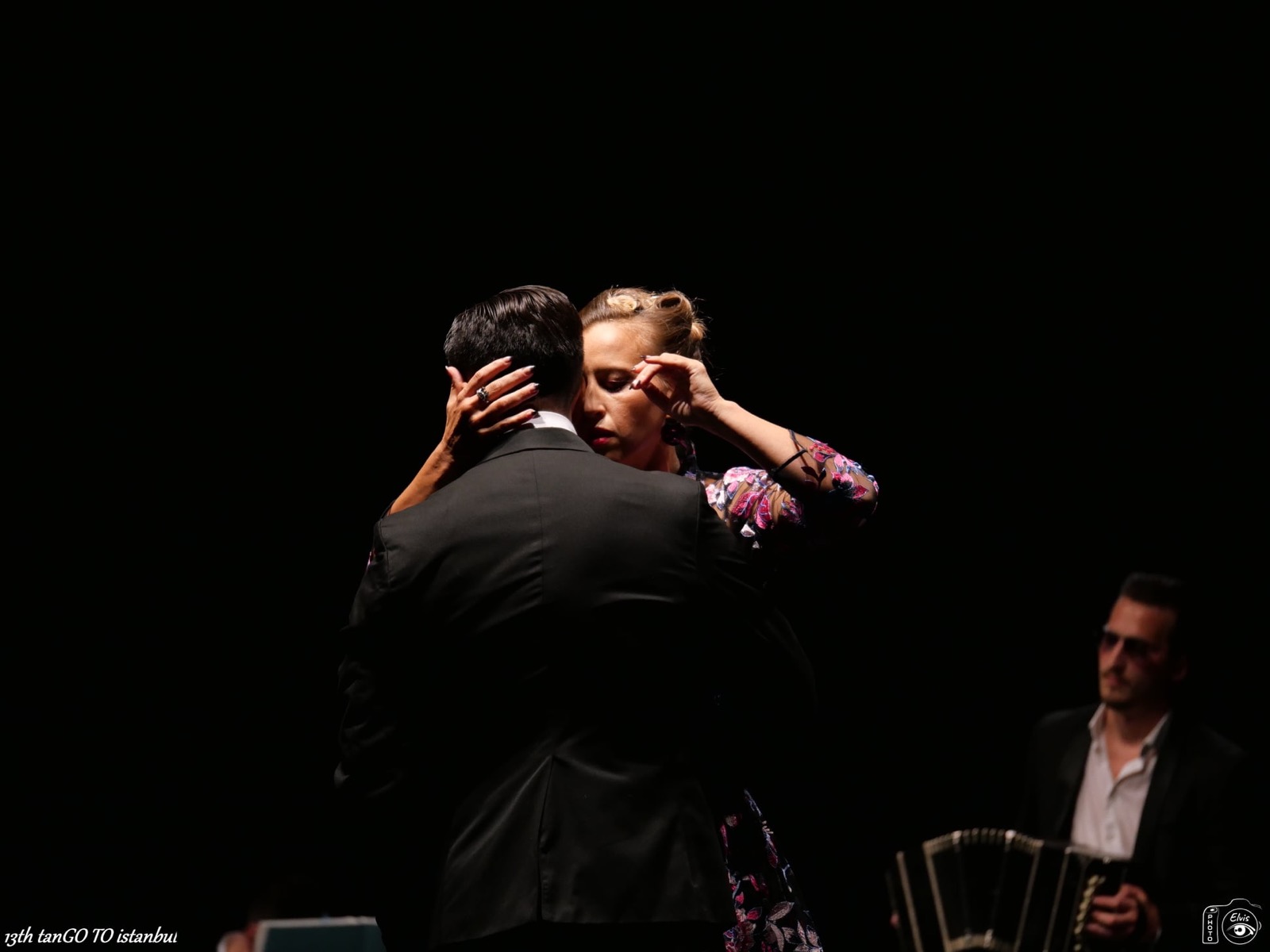 Ivan and Sara in an embrace on a dark stage with a bandoneon player